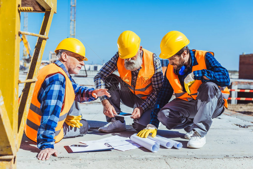 3名建筑工人坐在建筑工地的混凝土上讨论图片