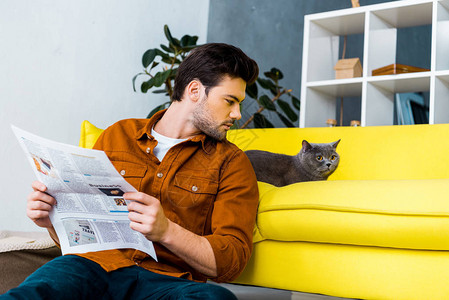 拿着报纸看猫的年轻人图片