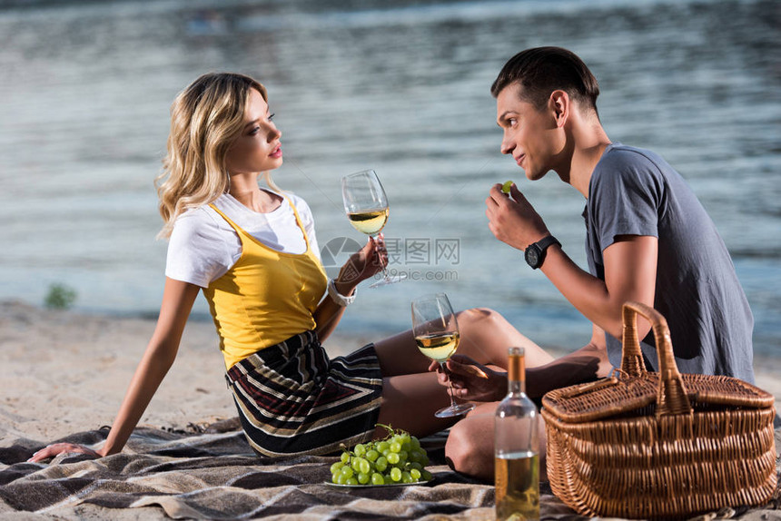 年轻夫妇晚上在河边海滩野餐时喝酒图片