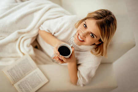 年轻微笑的女士在床上放松喝咖图片