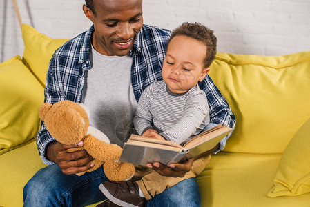 带着泰迪熊和小儿子读书的微笑的父亲背景图片