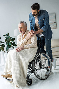 与在家轮椅的残疾老年父亲牵手的英俊图片