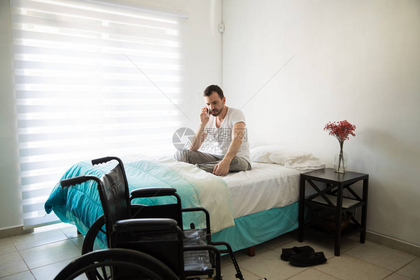 年轻的瘫痪男子坐在轮椅旁边的床上图片