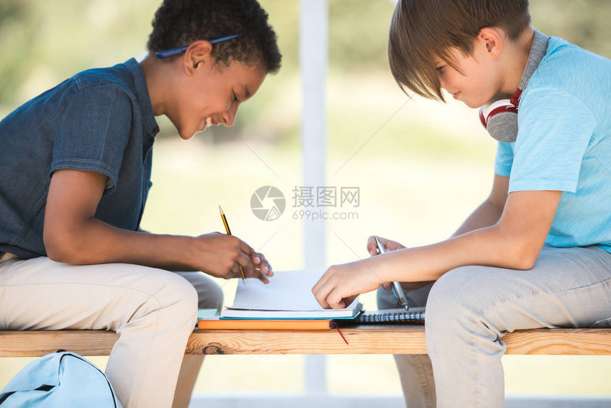 笑的多族裔少年男孩坐在长凳上一起学图片