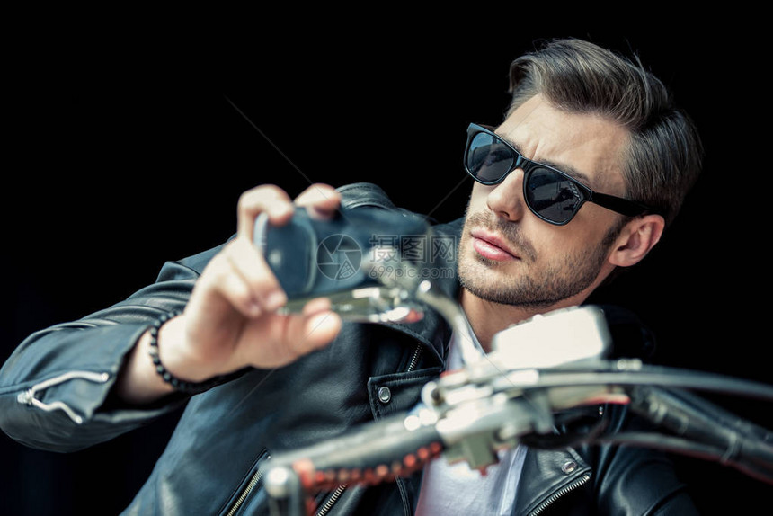 穿着太阳眼镜和皮夹克坐在摩托车上看远视的帅气图片