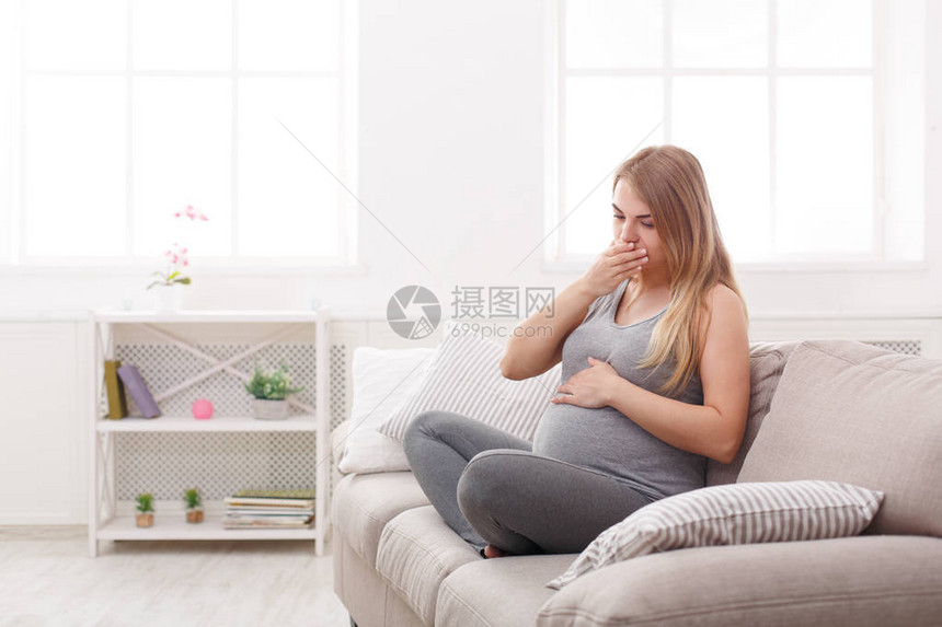 年轻呕吐女人坐在沙发上怀孕的金发女郎患有恶心怀孕症状期望图片
