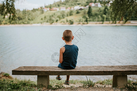 坐在湖边长椅上的内向男孩图片