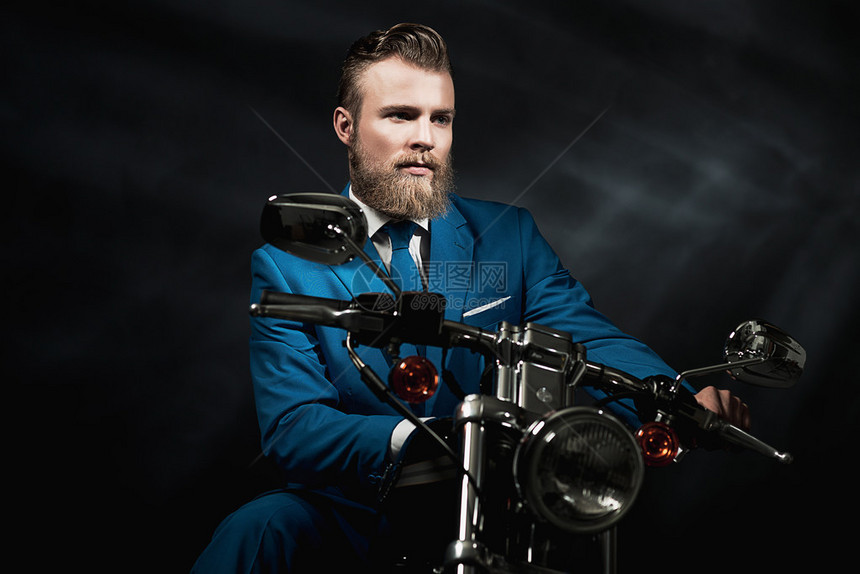 身着蓝色西装留着胡子的帅哥在黑暗中坐在摩托车上等着图片