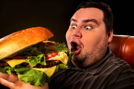 胖子节食失败吃快餐吃大汉堡的疯狂超重者的早餐垃圾餐导致黑色背景图片