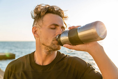 成年运动员锻炼后日出前在海边用健身瓶喝水图片