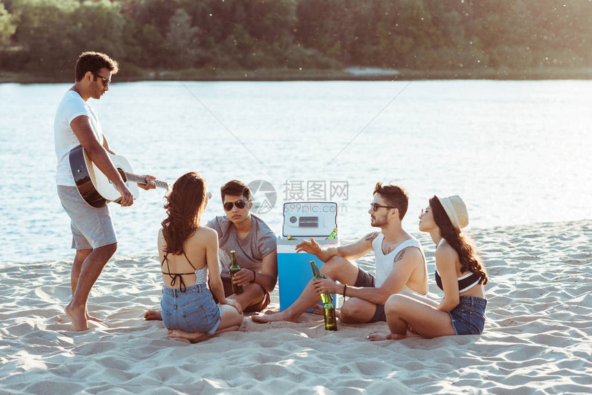 年轻朋友在沙滩上坐在一起喝啤酒图片