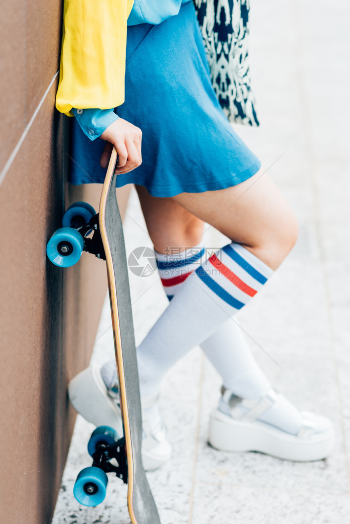 紧贴近的年轻偏心女人的手靠着墙靠着滑板运动图片