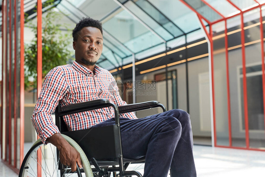 坐在办公大楼轮椅上的非洲青年残疾男子的肖像图片