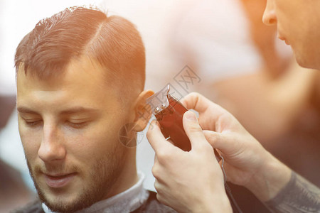 在理发店的美容厅里迷人的年轻男青年被理发师剪图片