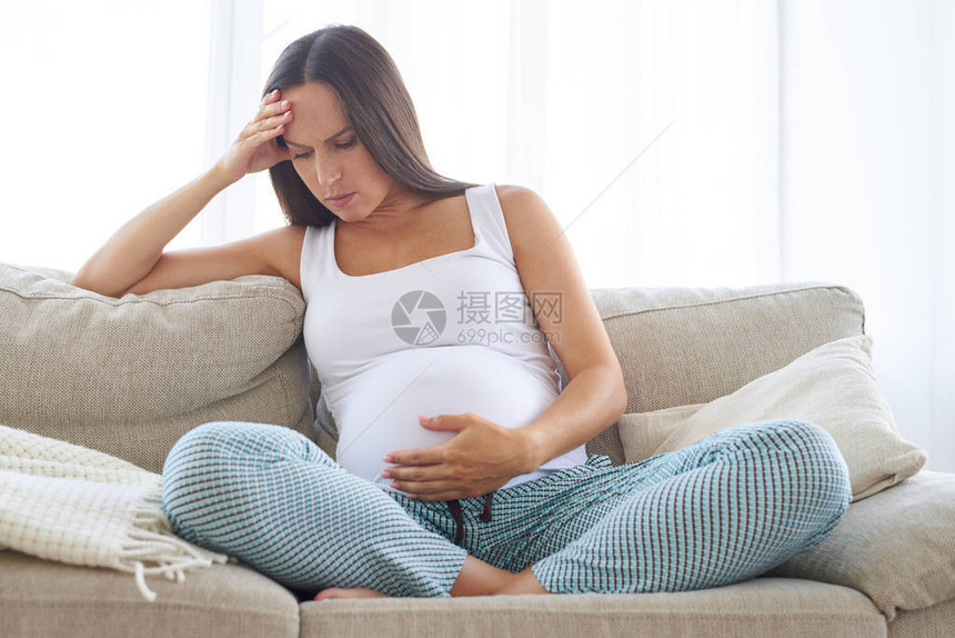 心烦意乱的孕妇头痛触摸她的腹部的特写图片