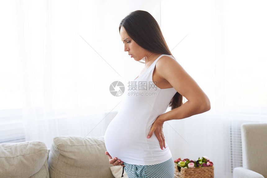 站在起居室的怀孕妇女背部疼痛降图片