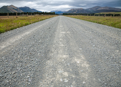 在新西兰直的砂石路穿过草场背景图片
