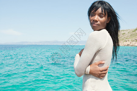 一位迷人的非洲裔美国年轻黑人女站在强烈的蓝色大海和晴朗的天空旁图片