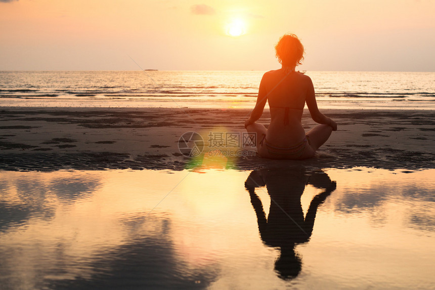 日落时坐在海滩上露着莲花的瑜伽妇女图片