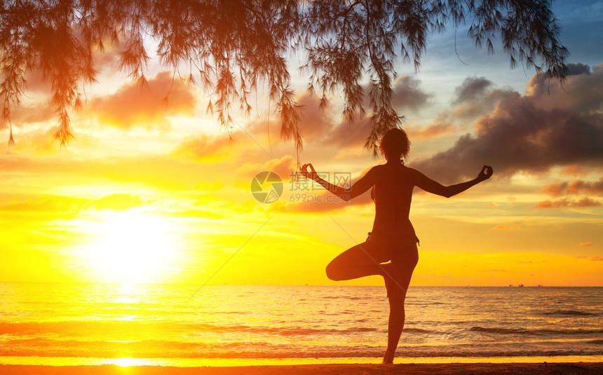 日落时在海滩上练习瑜伽的年轻女子剪影图片