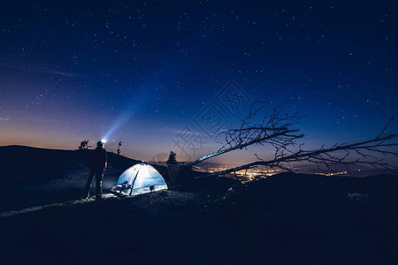 男人用他的手电筒把光指向天空山中的夜间营地星夜背景图片