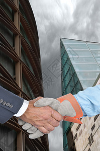 经理和工人在两座现代建筑前握手的特写镜图片