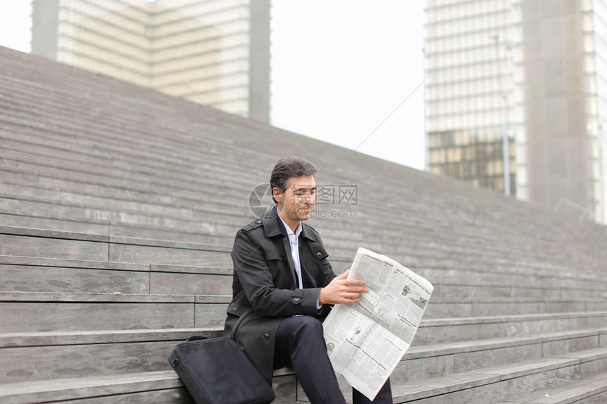 影响身着灰色外套的导师坐在梯级上阅读晨报文章取悦男人并引起微笑阅读任何好消息的男翻版积极情图片