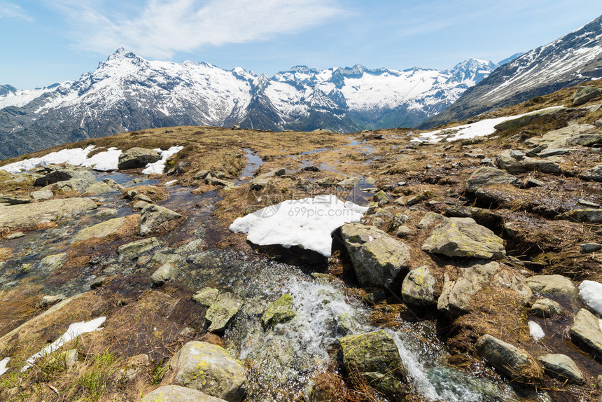 融化的雪在田园诗般的未受污染环境中流动的小山溪背景是白雪皑的山脉意大利阿尔卑斯山皮图片