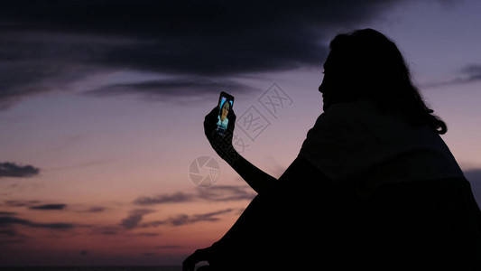 一个女孩的剪影使用智能手机在社交网络上进行直播图片