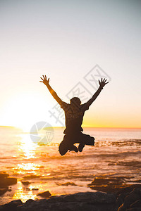 跳跃反对海滩地平线的年轻人剪影图片