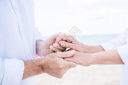 白衬衫中的高龄夫妇在蓝天下握着双手图片