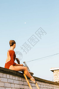 坐在城市建筑屋顶上用旧梯子坐着的年轻漂图片