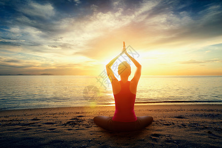 日落时在沙滩上练习瑜伽的剪影年轻女子图片