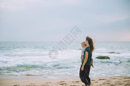 年轻母亲在沙海滩抱着可爱的小女图片