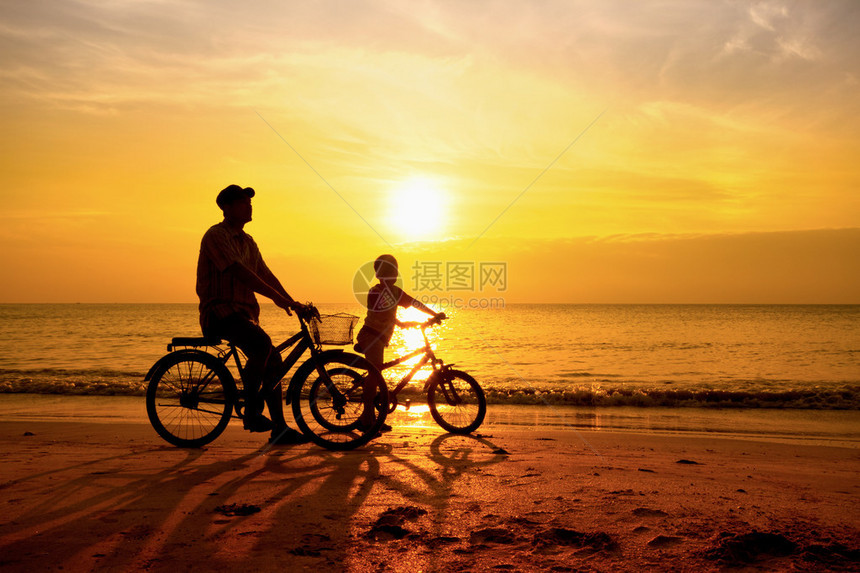 太阳升起时父亲和儿子在海滩上骑自行车图片