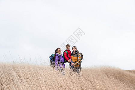 幸福的家庭与背包站在高的干草地上面背景图片