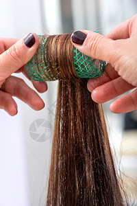 美发师将客户的棕色长发卷在发器或卷发器上图片