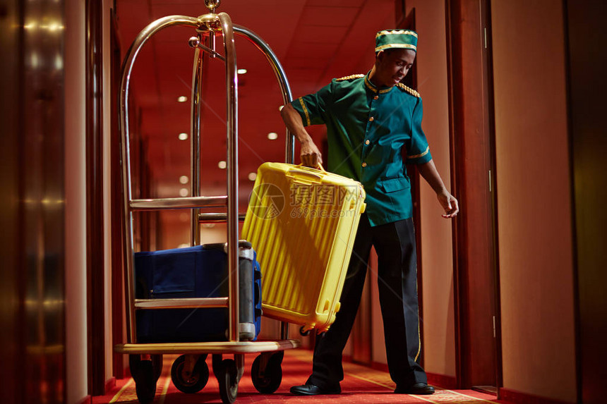 将行李袋带到客房的非洲侍者肖像和在旅馆走廊上装着行李图片