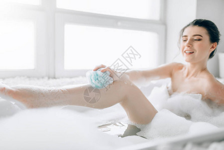 年轻妇女在洗澡时使用海绵并配有泡沫图片