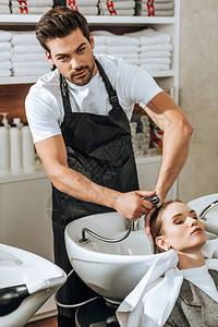 英俊的年轻美发师在美容院向女人洗头发图片