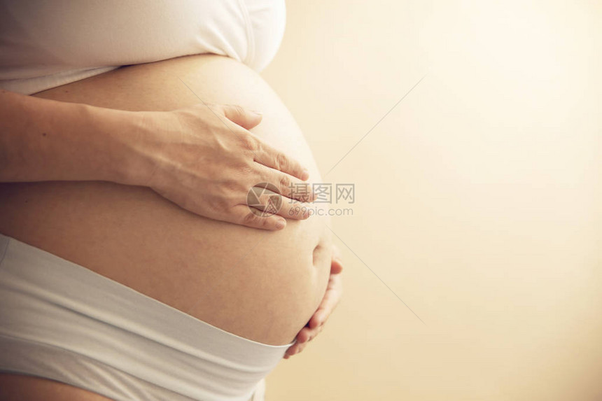 年轻怀孕妇女将手握在她肿胀的肚子上准备和期望概念闭紧水图片