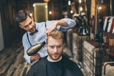 年轻的理发师在理发店用吹风机吹干顾客的头发图片