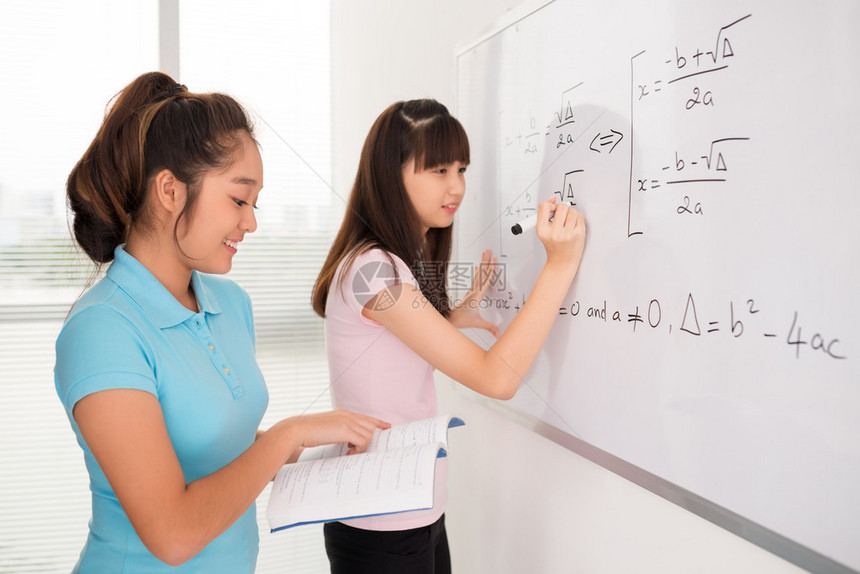 亚洲女学生从白板代数手册中写出方程式图片