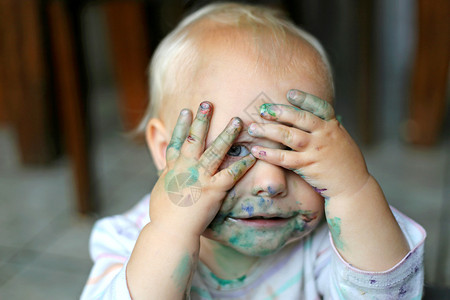 一个小孩女涂满了乱七八糟的油漆用手盖住背景图片