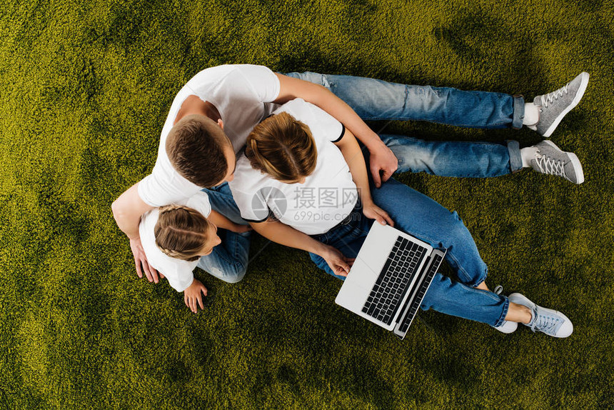 带着笔记本电脑躺在绿色草坪上的家庭俯视图图片