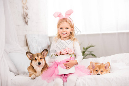 穿着兔子耳朵的可爱孩子头带和WelshCorgi狗坐在一起在家里床上图片