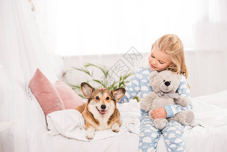 可爱的孩子坐在床上和PembrokewelshCorgi狗和图片