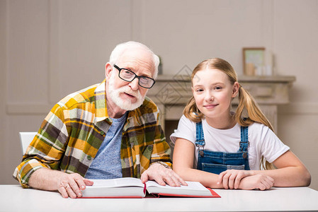 祖父和孙女坐在桌边拿着书图片