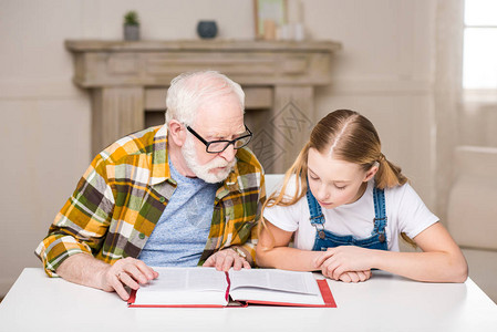 祖父和孙女一起坐在桌边看书图片