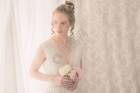 一位年轻漂亮的新娘在她的白色房间里拿着一束玫瑰花的半身照背景图片